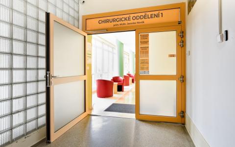 otevřené křídlo oranžových matně prosklených protipožárních dveří s nadsvětlíkem, chodba nemocnice