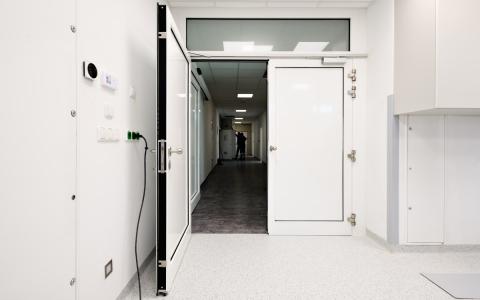 otevřené křídlo bílých protipožárních dveří s proskleným nadsvětlíkem, chodba nemocnice